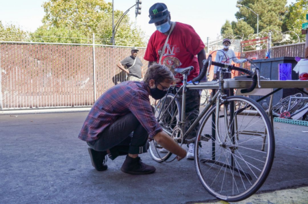 one person watching a second person fixing a bicycle